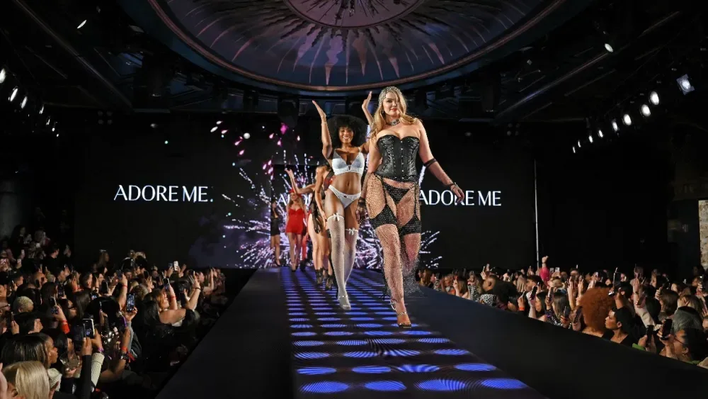 A model walks the Runway 7 catwalk inside Sony Hall beneath an Adore Me screen