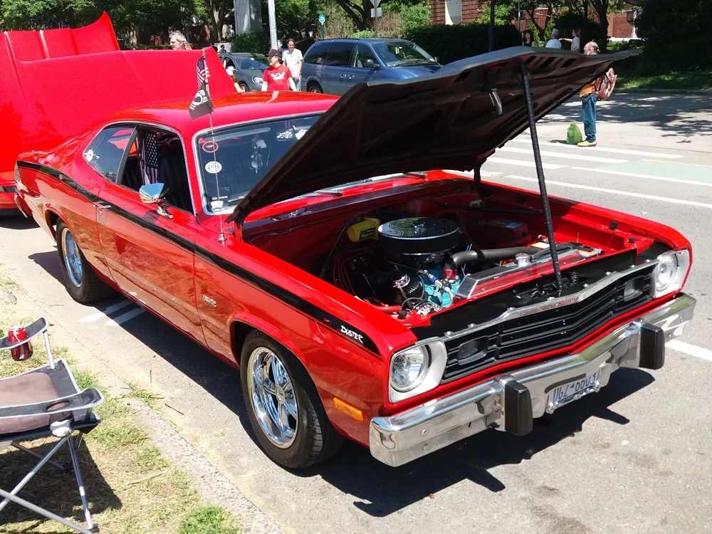 A polished red Plymouth Duster is displayed with its hood open beside Shore Boulevard