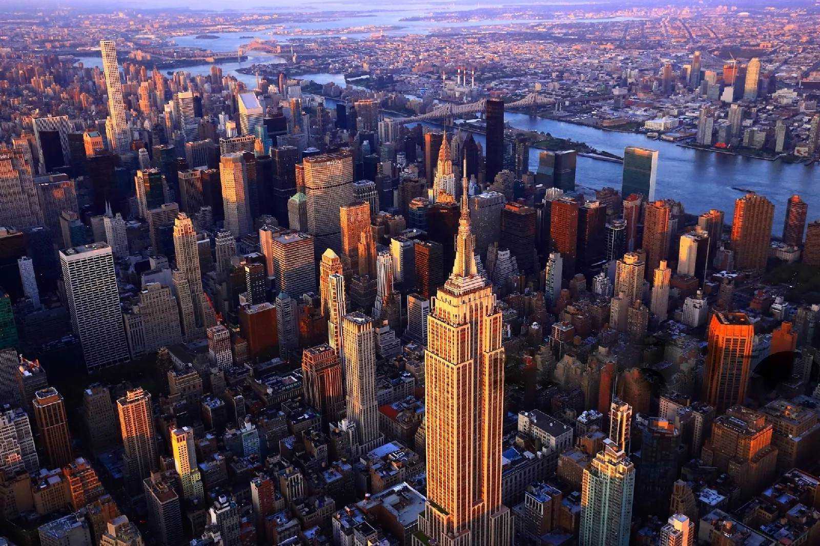 An aerial view of the Empire State Building and the surrounding Midtown Manhattan skyline at sunset