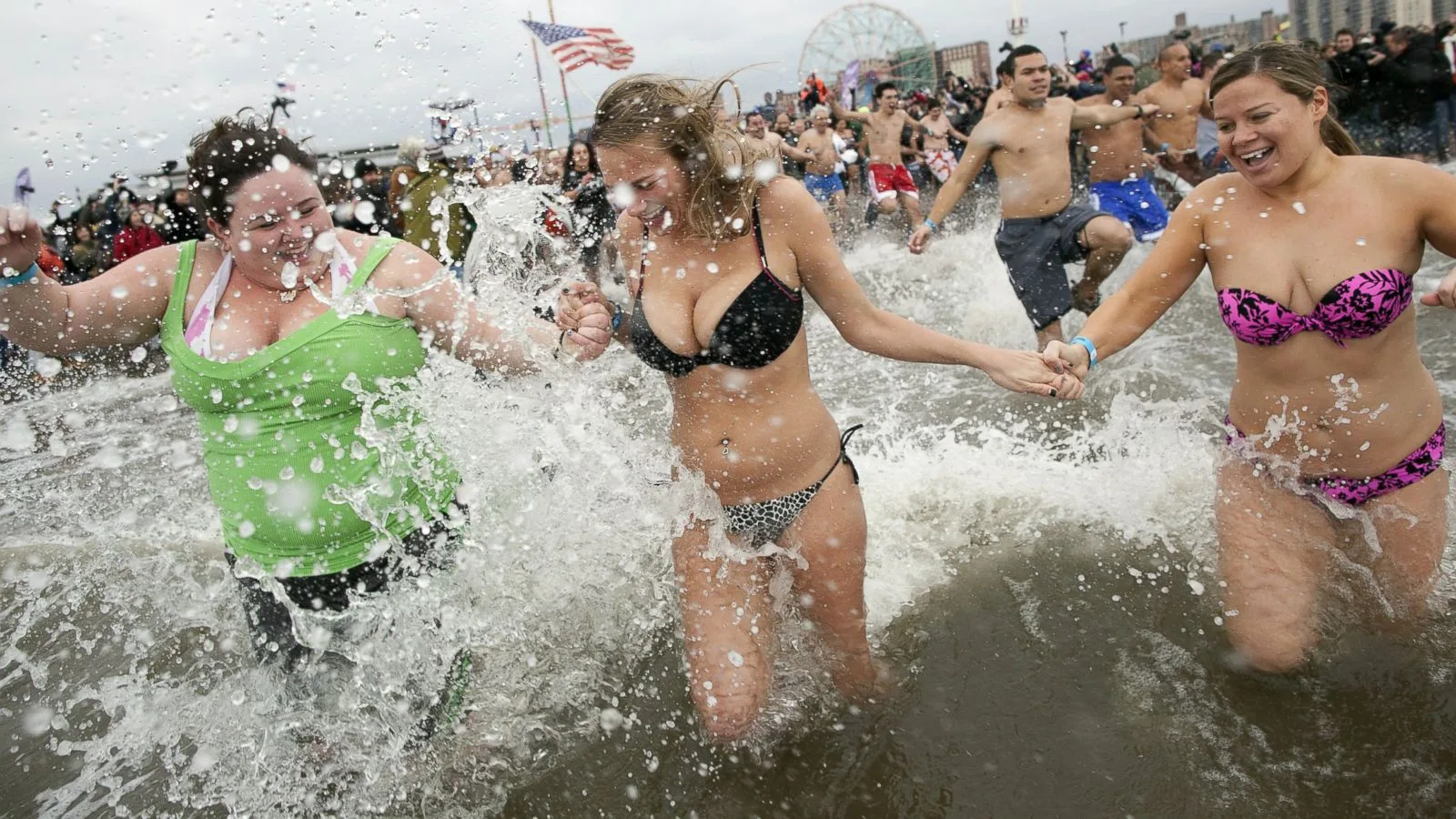 Swimmers hold hands as they run through a breaking wave at Coney Island on New Year's Day