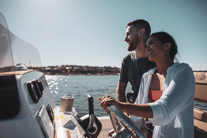 A woman steers a motorboat while a man sits beside her on open water