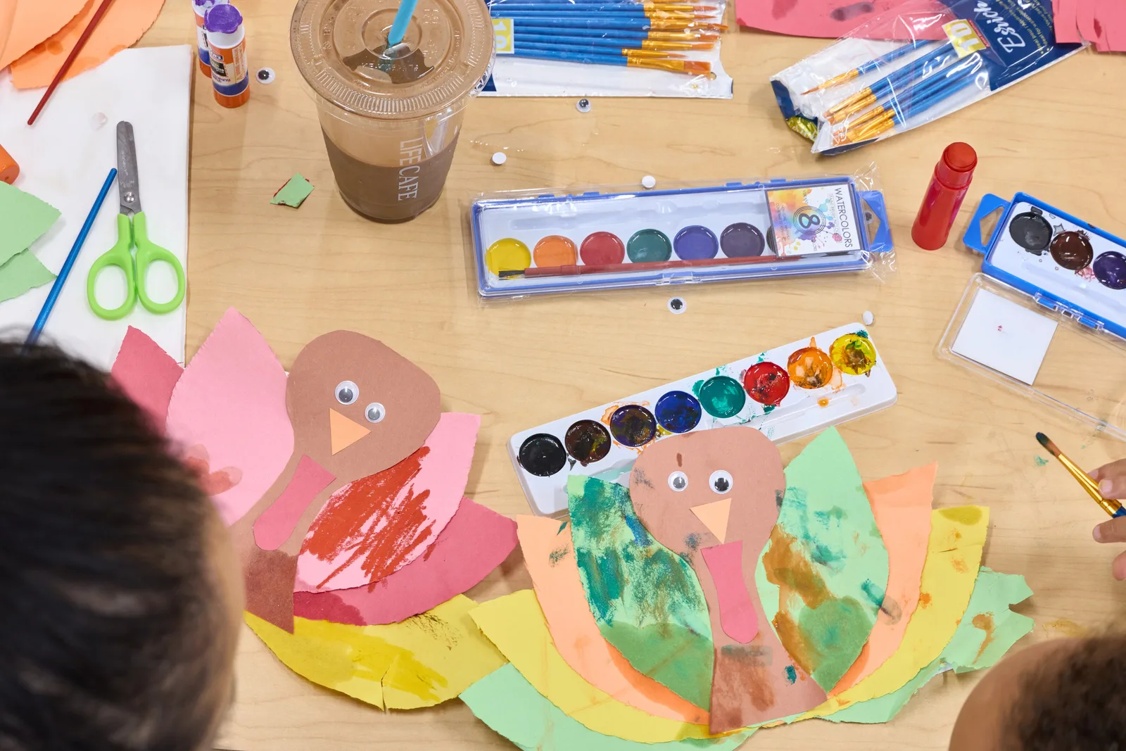 Children making colorful paper turkeys with watercolor paints, brushes and craft supplies