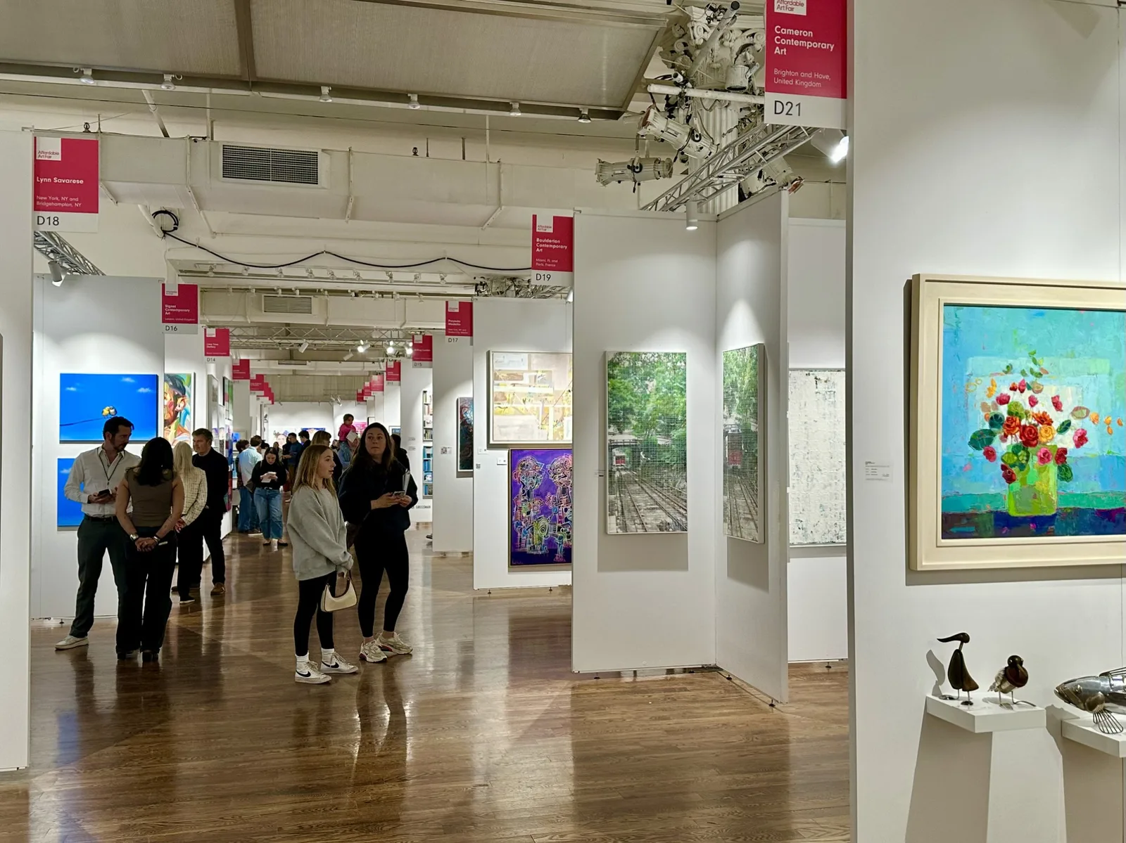 Visitors walk through white gallery booths filled with contemporary paintings and sculpture