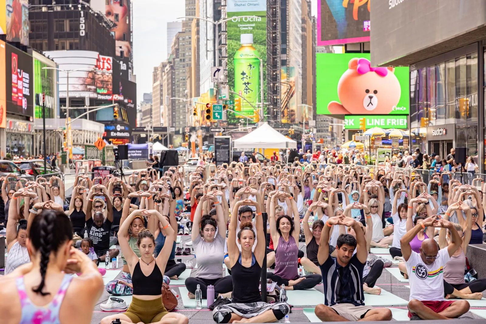 Hundreds of yoga participants raise their arms while seated on mats in Times Square