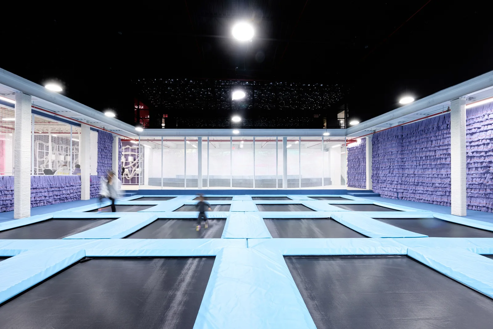 Children moving across a large grid of blue-framed trampolines inside Space Club DUMBO