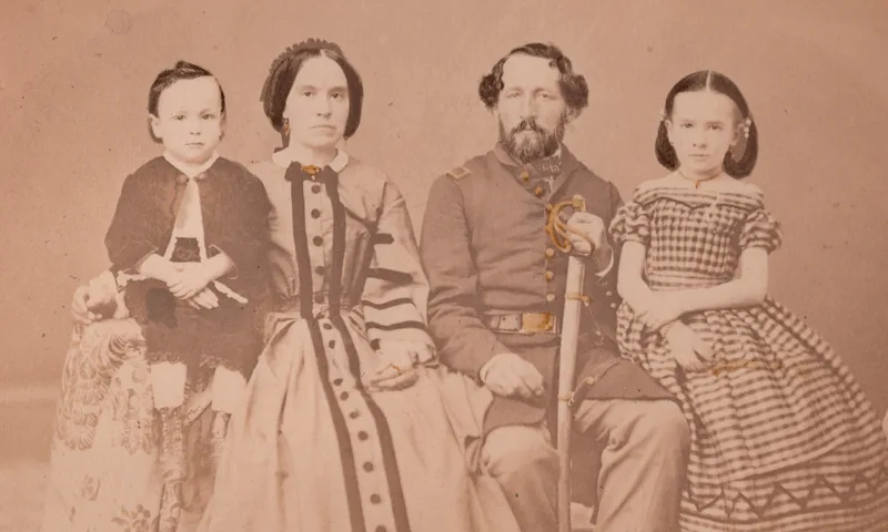 A sepia-toned vintage photograph of a family of four all dressed in 19th-century clothing.