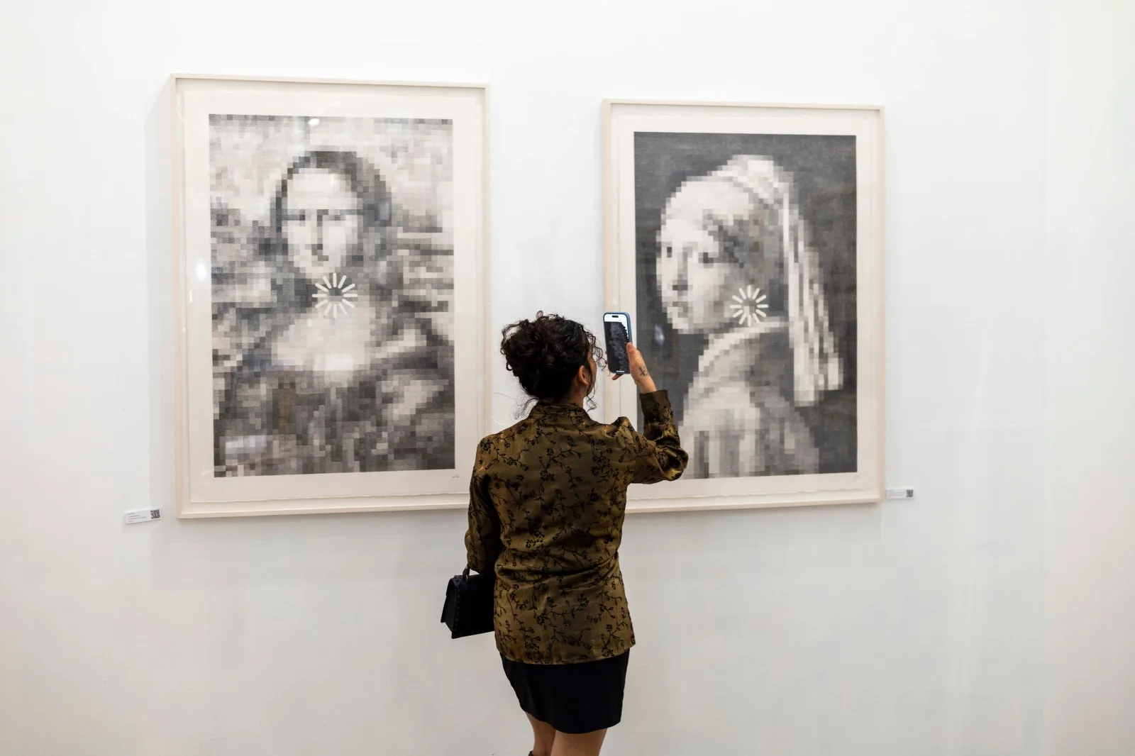 A visitor photographs pixelated drawings of the Mona Lisa and Girl with a Pearl Earring