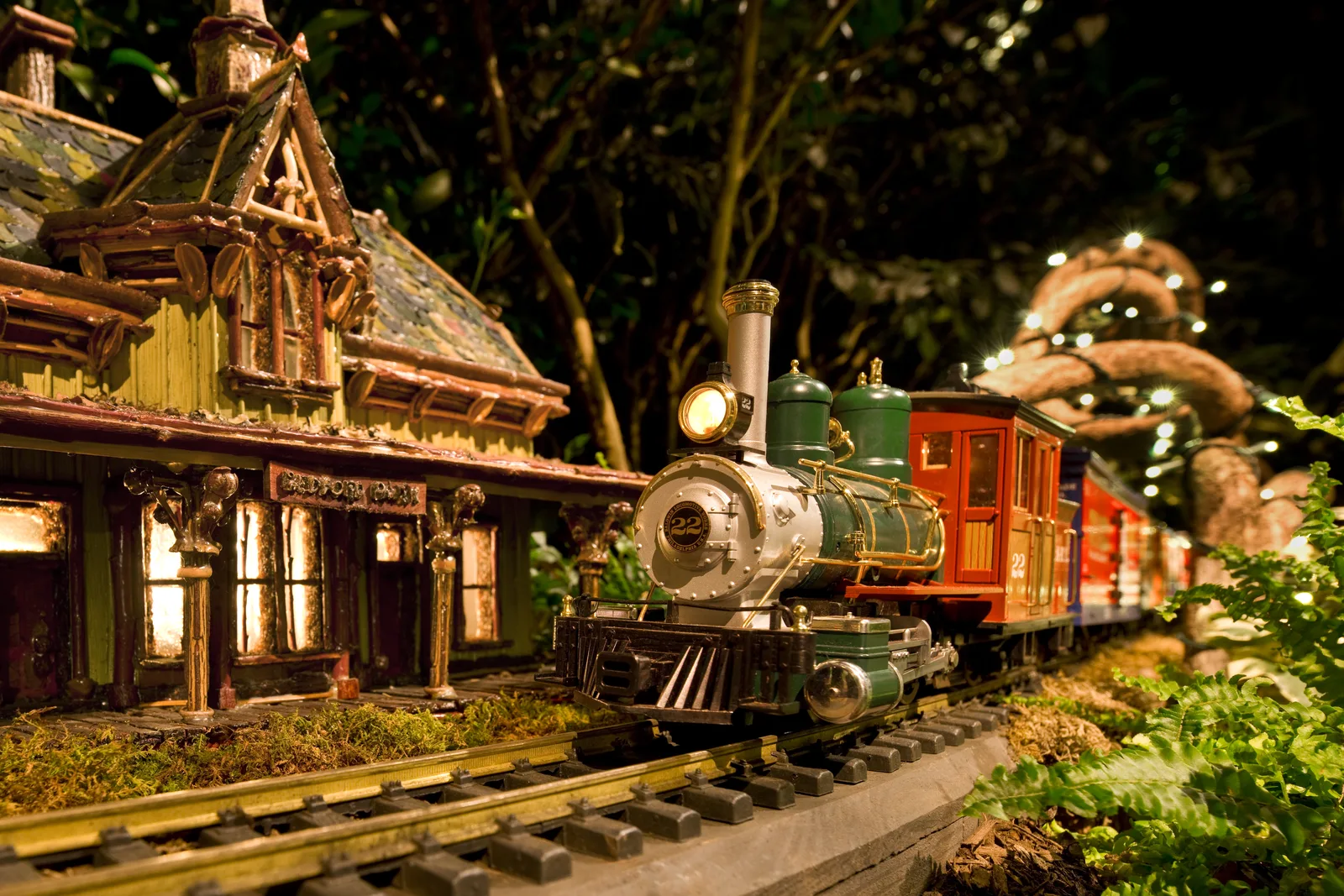 A green and silver model steam locomotive passes a miniature station built from plant materials at the NYBG Holiday Train Show