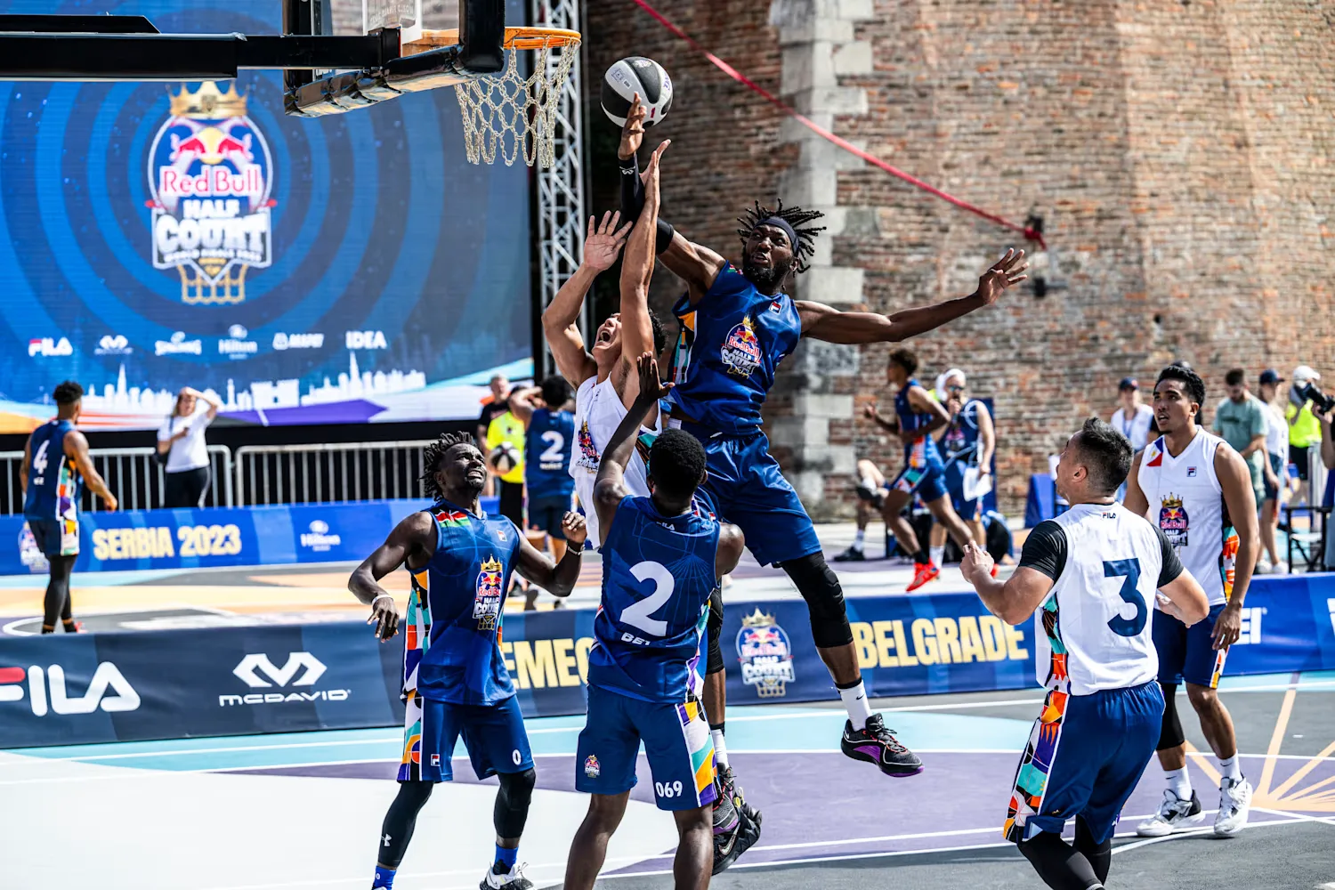 Three-on-three basketball players compete on a colorful outdoor court beside the Brooklyn waterfront