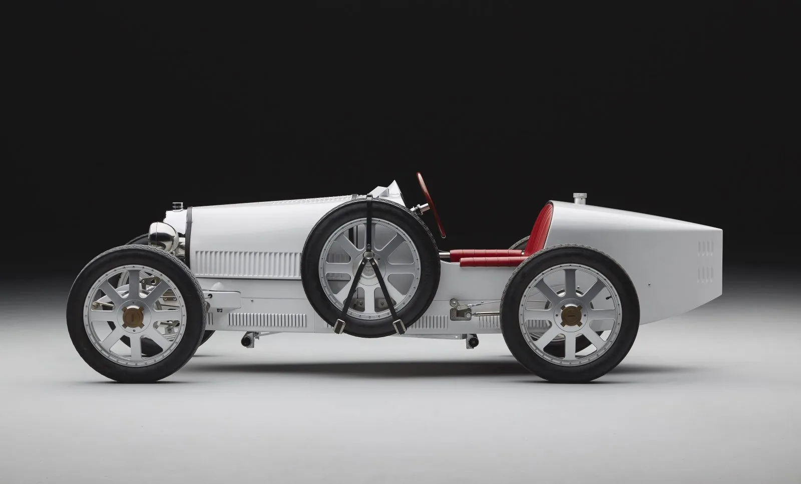 A silver scaled Bugatti recreation with red seats shown in profile against a dark background