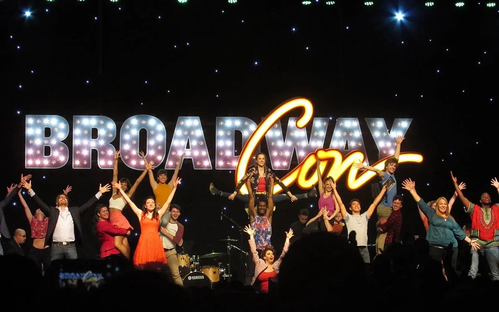 BroadwayCon guests raise their arms onstage beneath the illuminated convention logo