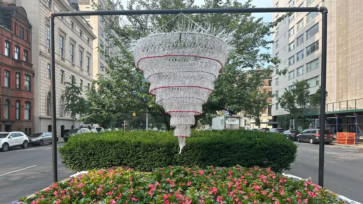 A monumental chandelier made from clear plastic water bottles suspended above flowers in the Park Avenue median