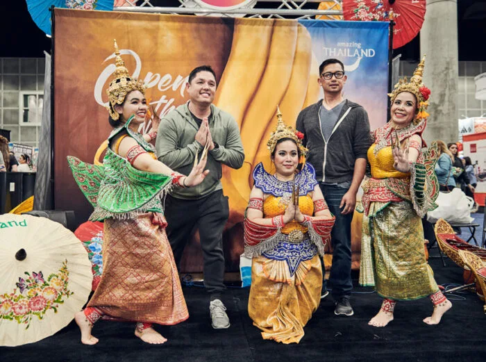 Four performers in colorful Thai dress pose with two attendees at the New York Travel Show