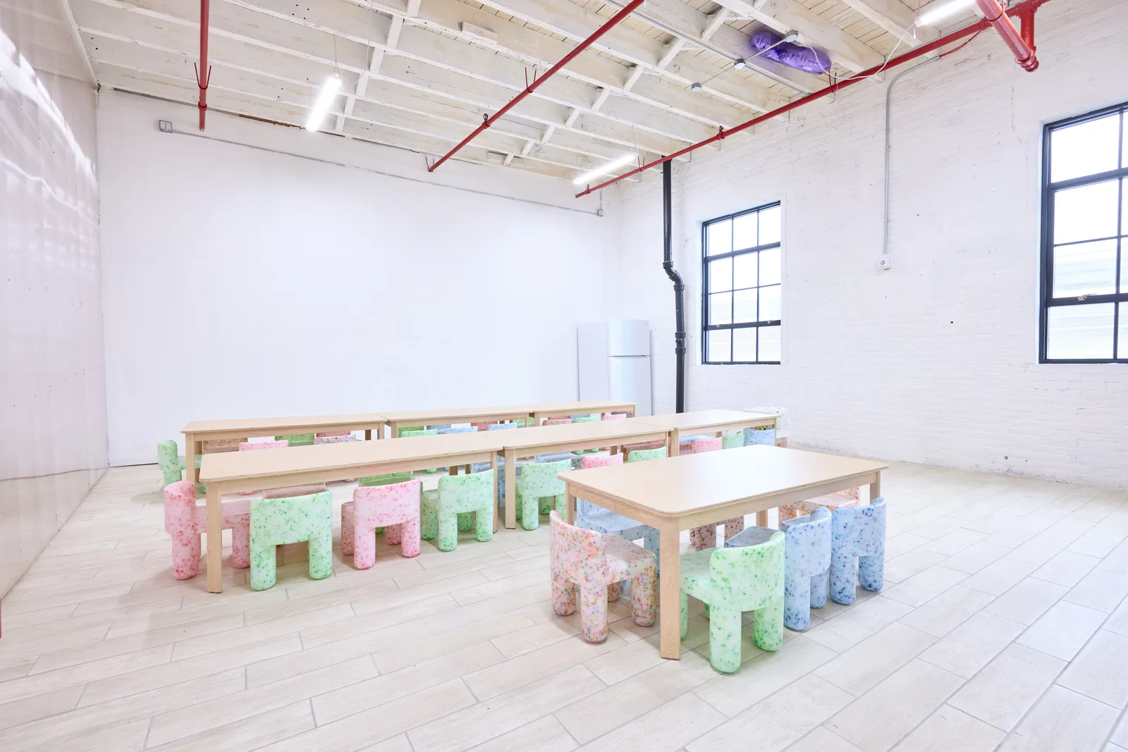 A bright classroom at Space Club DUMBO with child-sized wooden tables and multicolored chairs