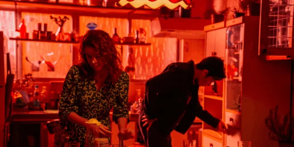 In this red-hued photographic image, two people are occupied with domestic chores