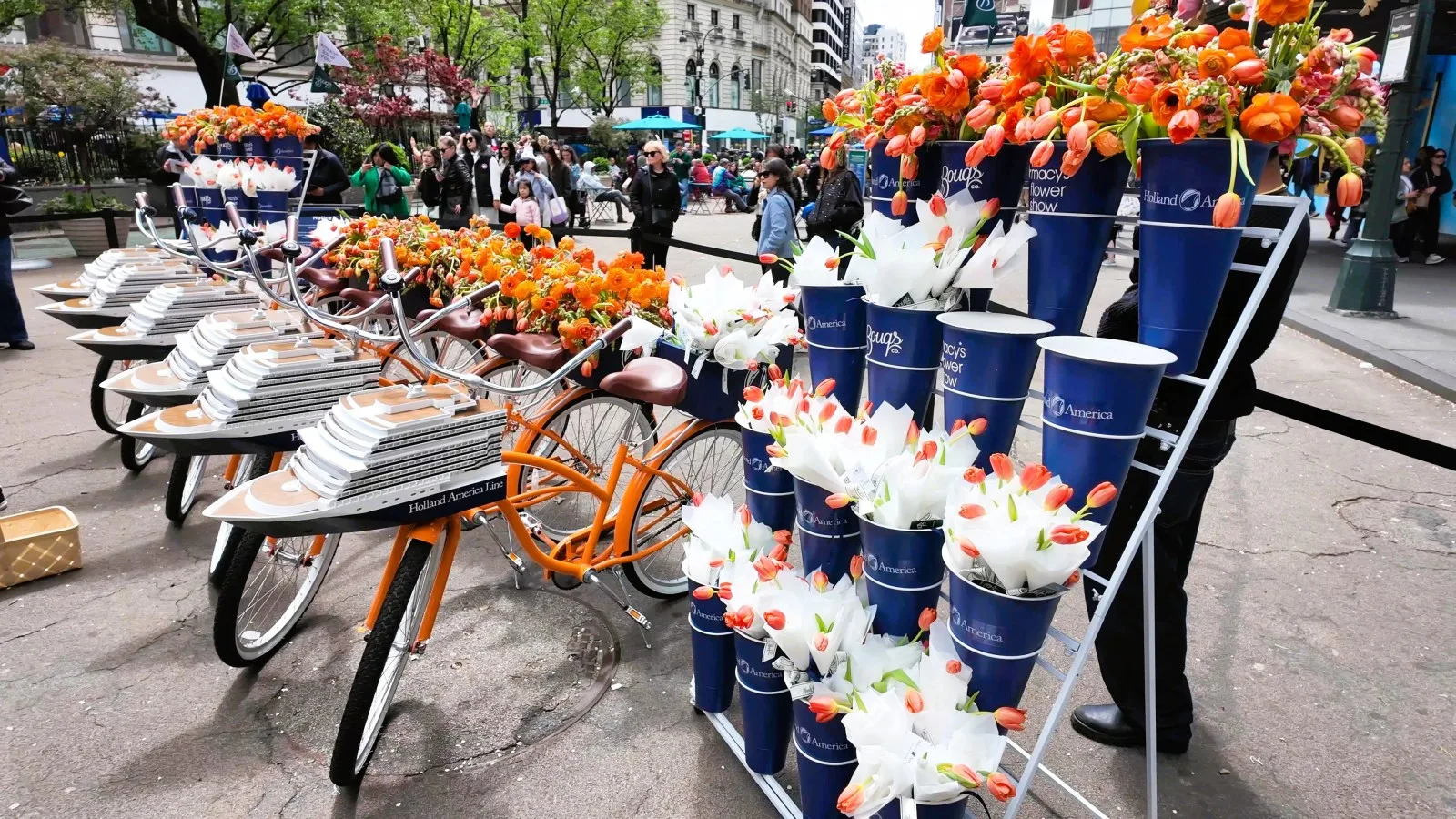 Orange bicycles and tiered blue buckets display orange and white tulips outside Macy's