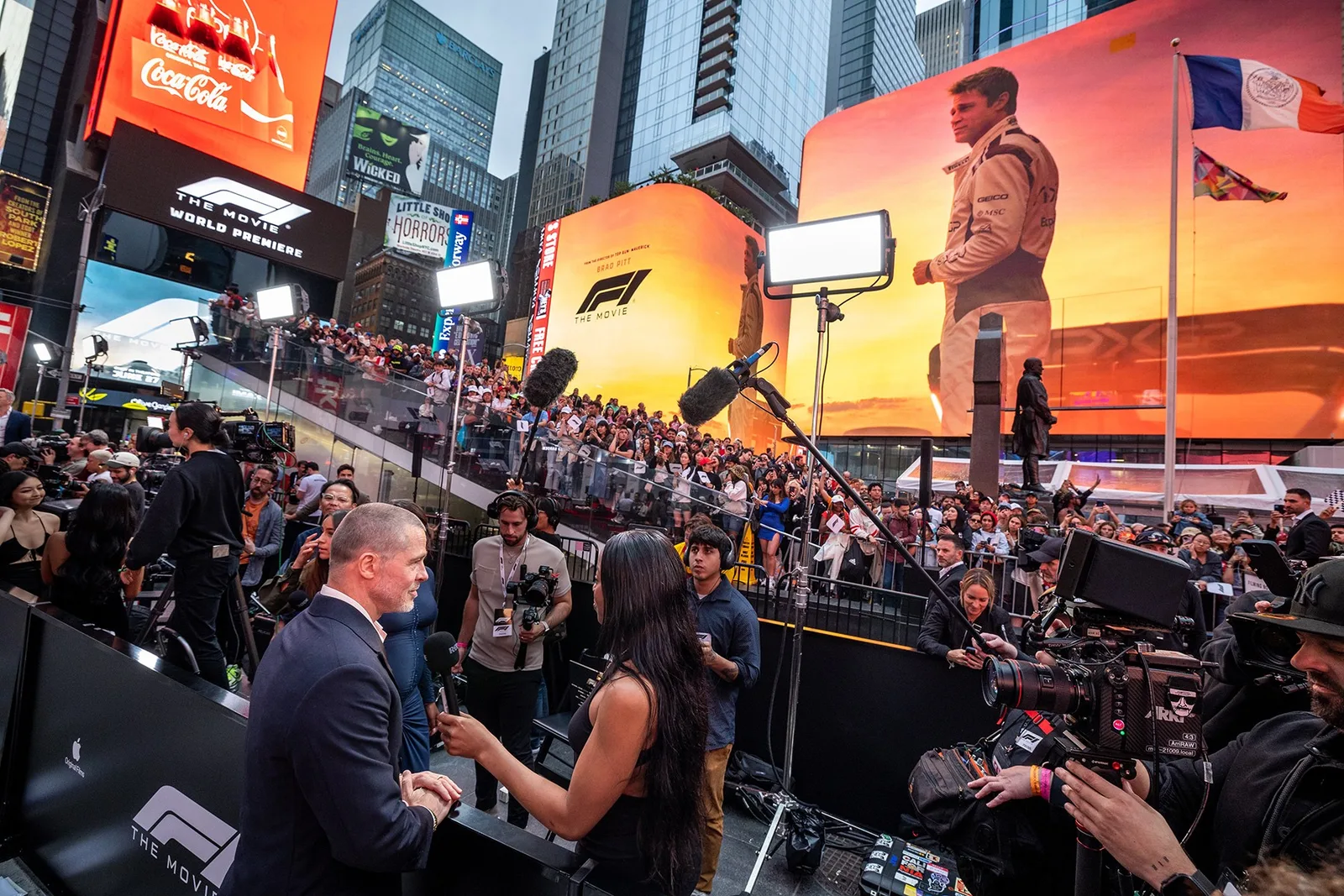 A reporter interviews a guest as crowds gather beneath F1 movie billboards in Times Square