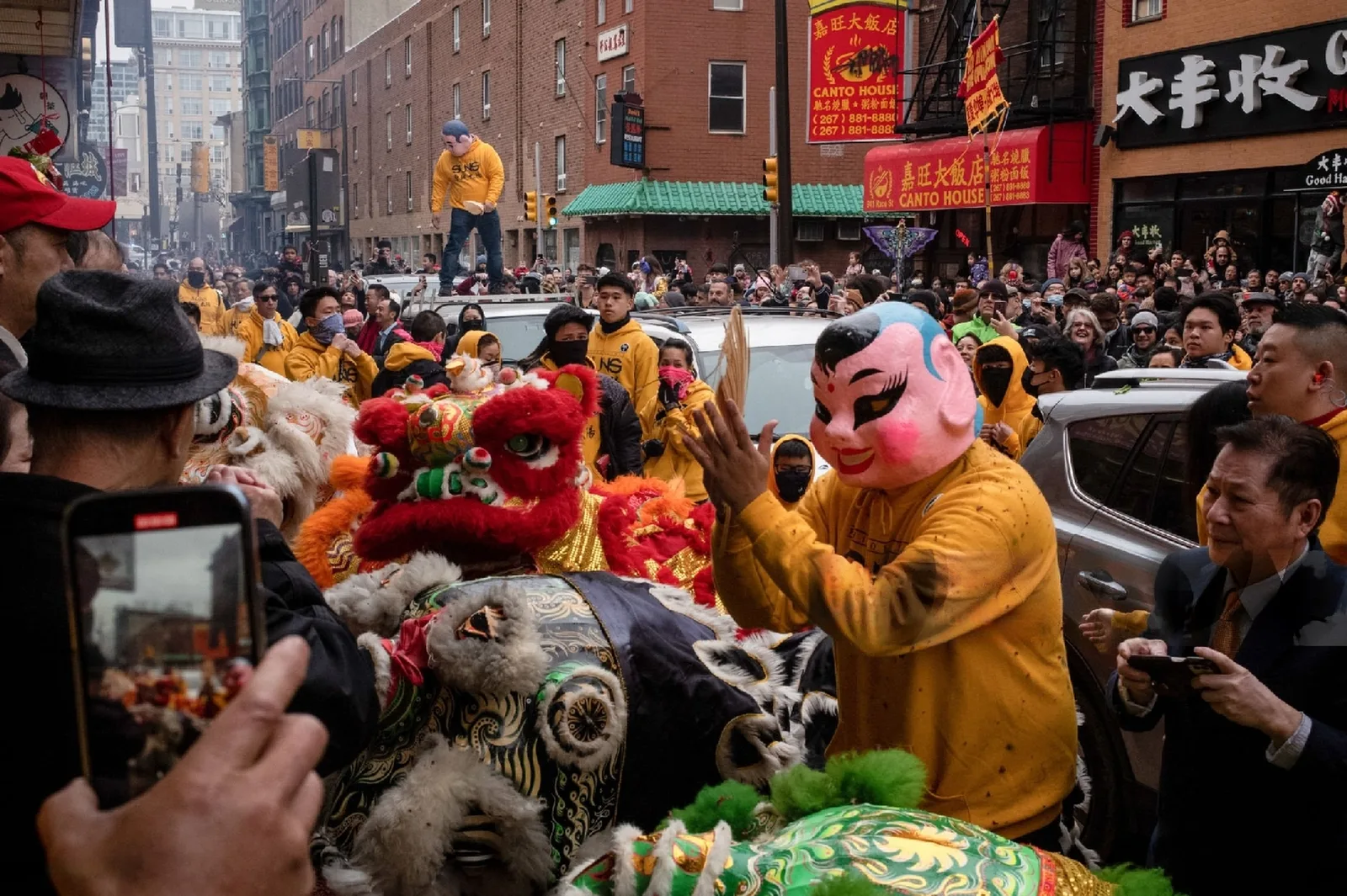 A colorful lion dance costume moves through a crowded Chinatown street