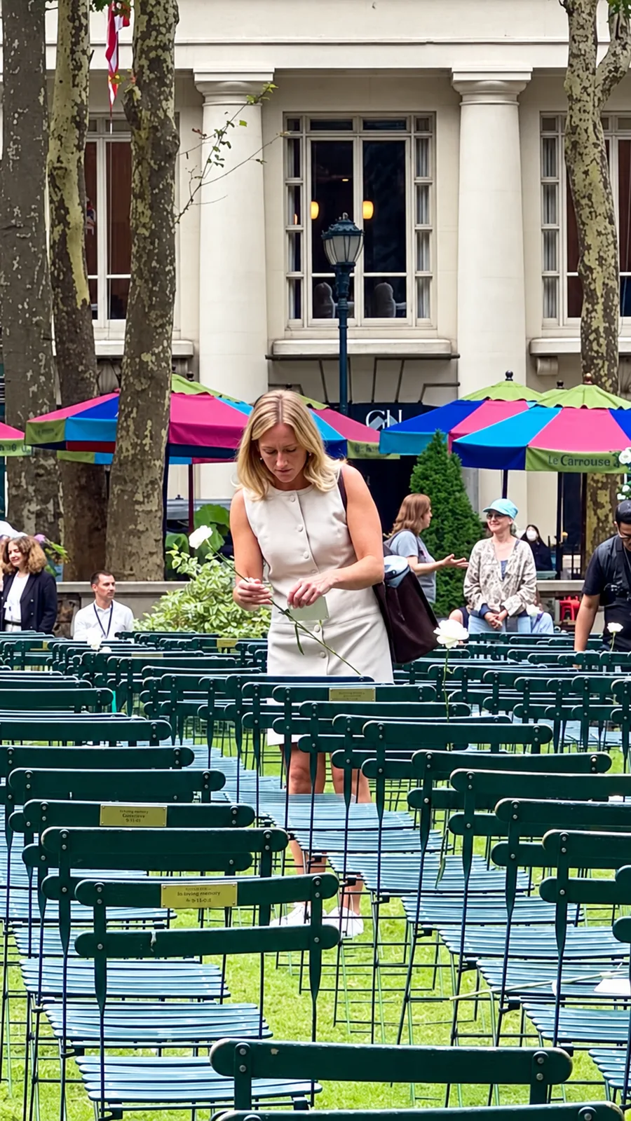 A visitor holds a white flower among rows of empty green chairs on the Bryant Park lawn.