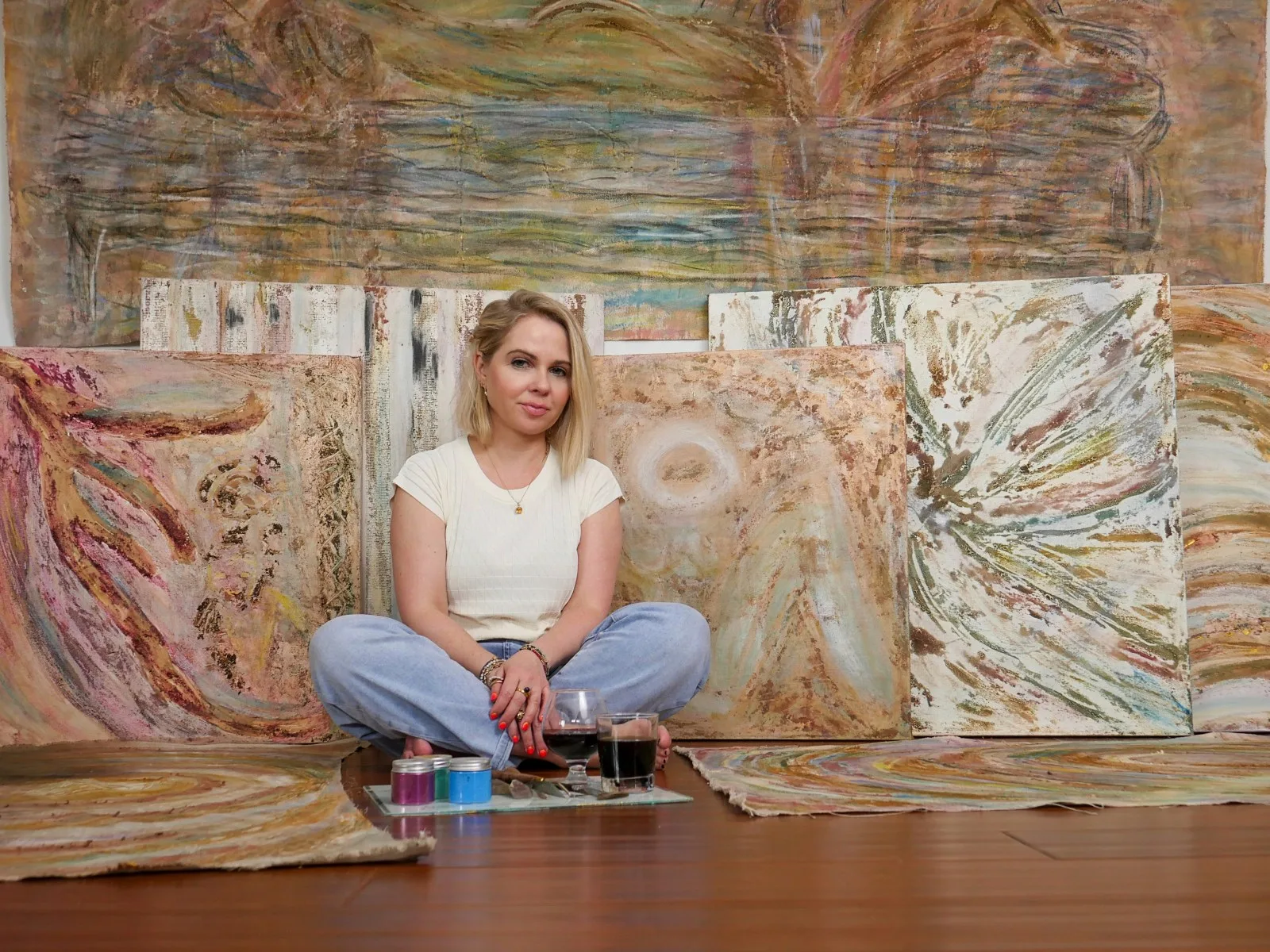 Artist Kasia Muzyka sits among earth-toned abstract paintings and natural pigments