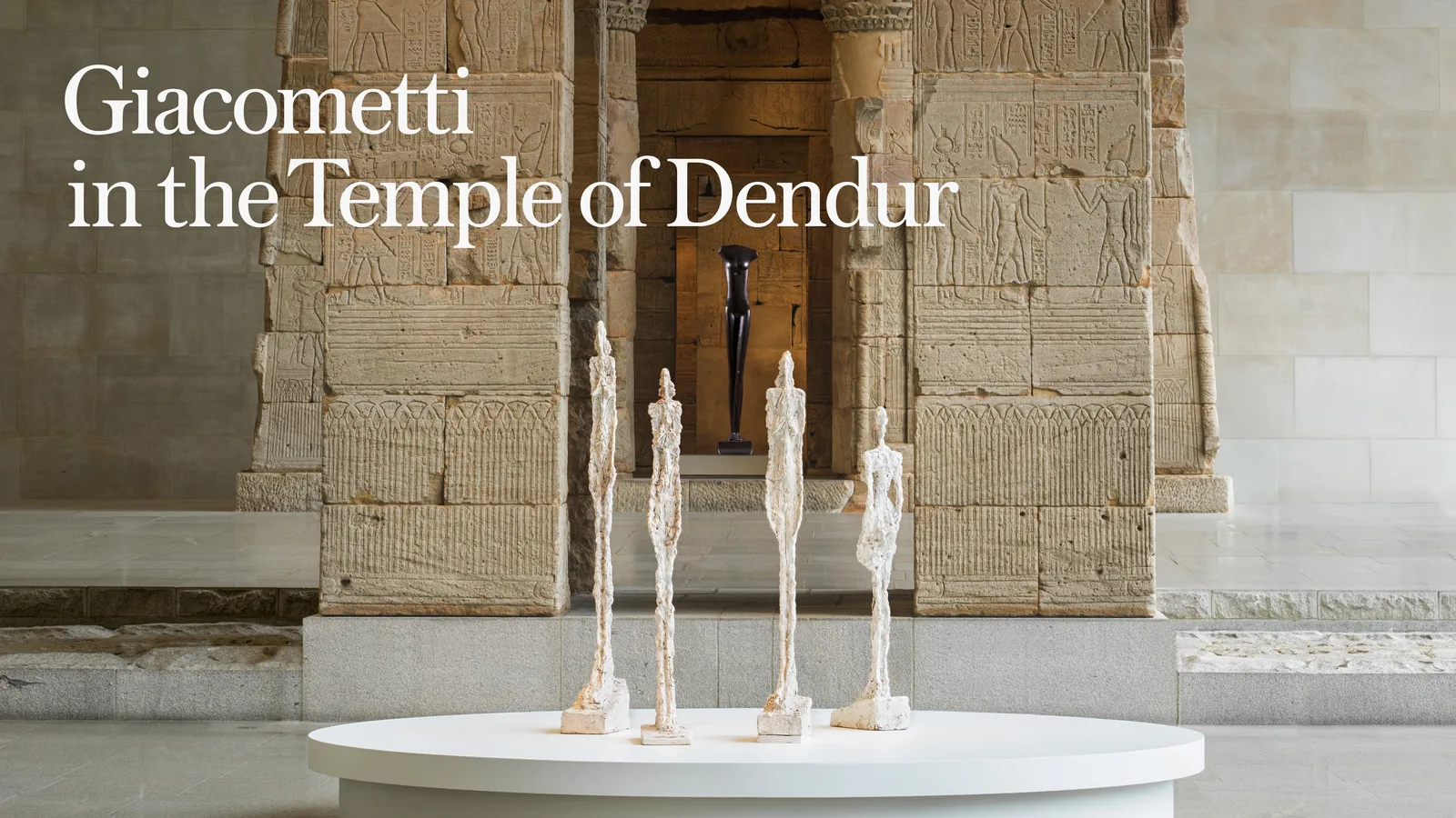 Tall, slender sculpture by Giacometti stands against a dark teal background. Text reads "Giacometti in the Temple of Dendur," suggesting an exhibit.