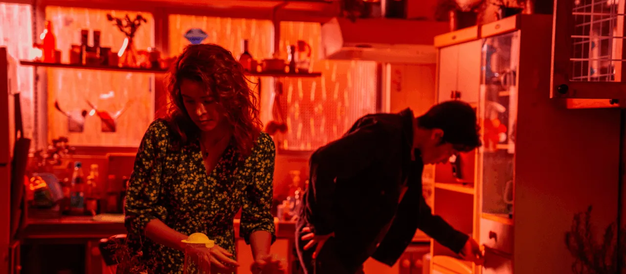 In this red-hued photographic image, two people are occupied with domestic chores